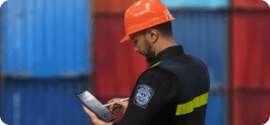 customs worker in front of containers looking down at a clipboard