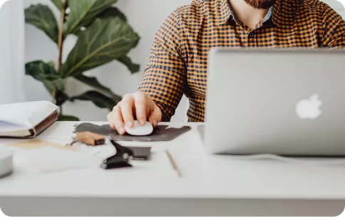 man waring a plad shirt with in front of a desk looking at a laptop