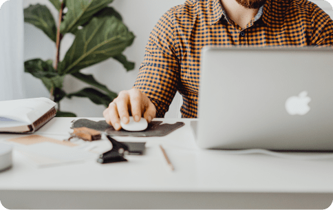 man waring a plad shirt with in front of a desk looking at a laptop