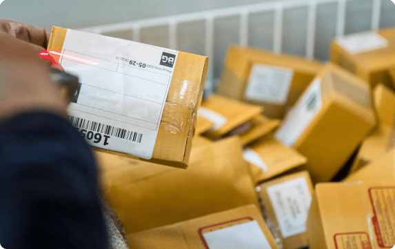 a pile of packages in a basket with a person holding one of the packages and scanning it